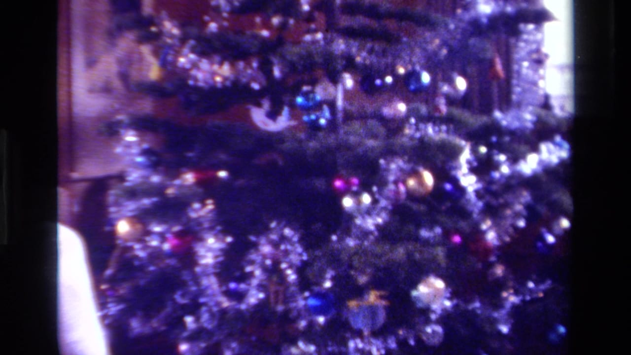 1979 California 8mm frame showing a Christmas tree covered in tinsel, ornaments, and colored lights inside a dim home setting.