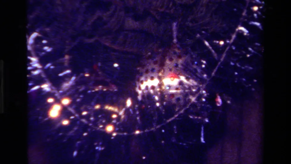 1979 California 8mm frame showing a darker close-up of tinsel, evergreen branches, a reflective silver ornament, and warm tree lights.