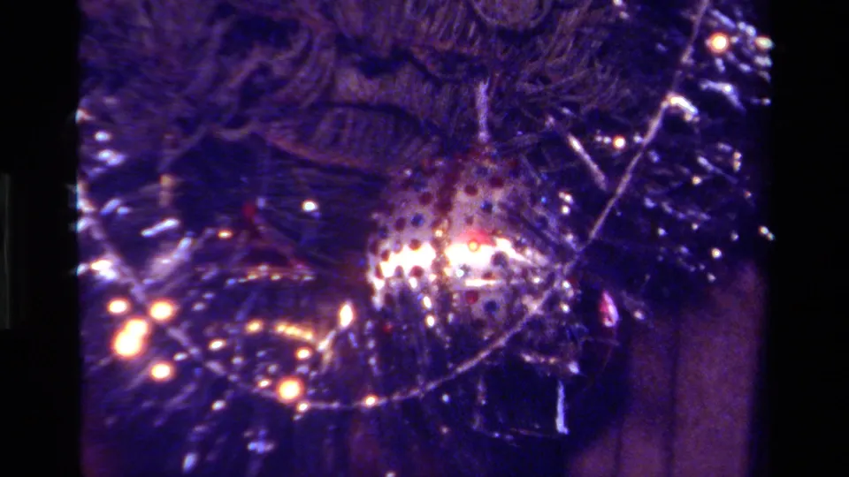 1979 California home-movie frame of a decorated Christmas tree, focused on tinsel, evergreen branches, a shiny ornament, and small lights.