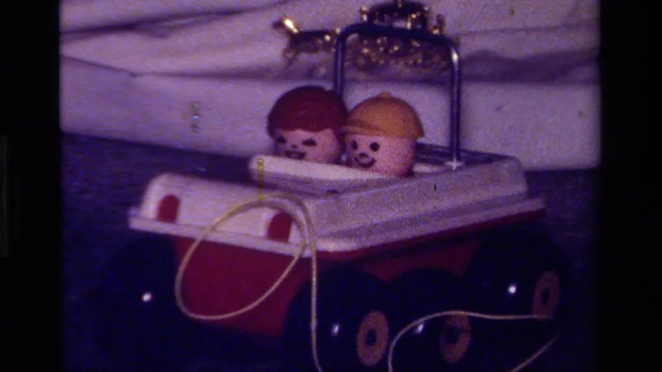 1979 California 8mm frame showing a red and white toy car with two small figurines seated inside.