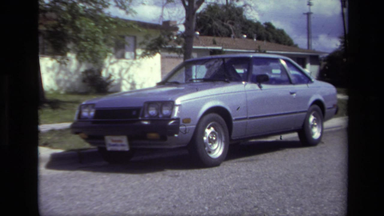 A silver late-1970s coupe sits curbside on a Laguna Beach residential street, with houses and trees behind it.