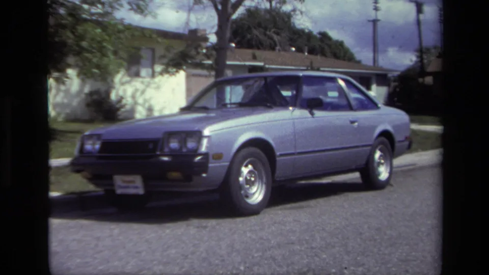 The car is shown in a wider side view on a Laguna Beach street, with curb, lawn, and residential buildings visible.