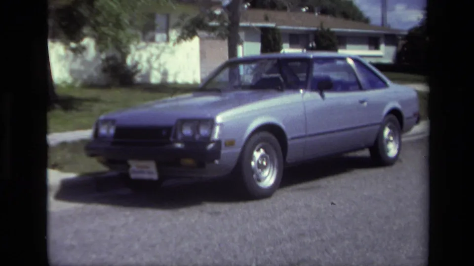 A silver late-model car remains parked curbside in 1979 Laguna Beach, framed with houses and trees behind it.