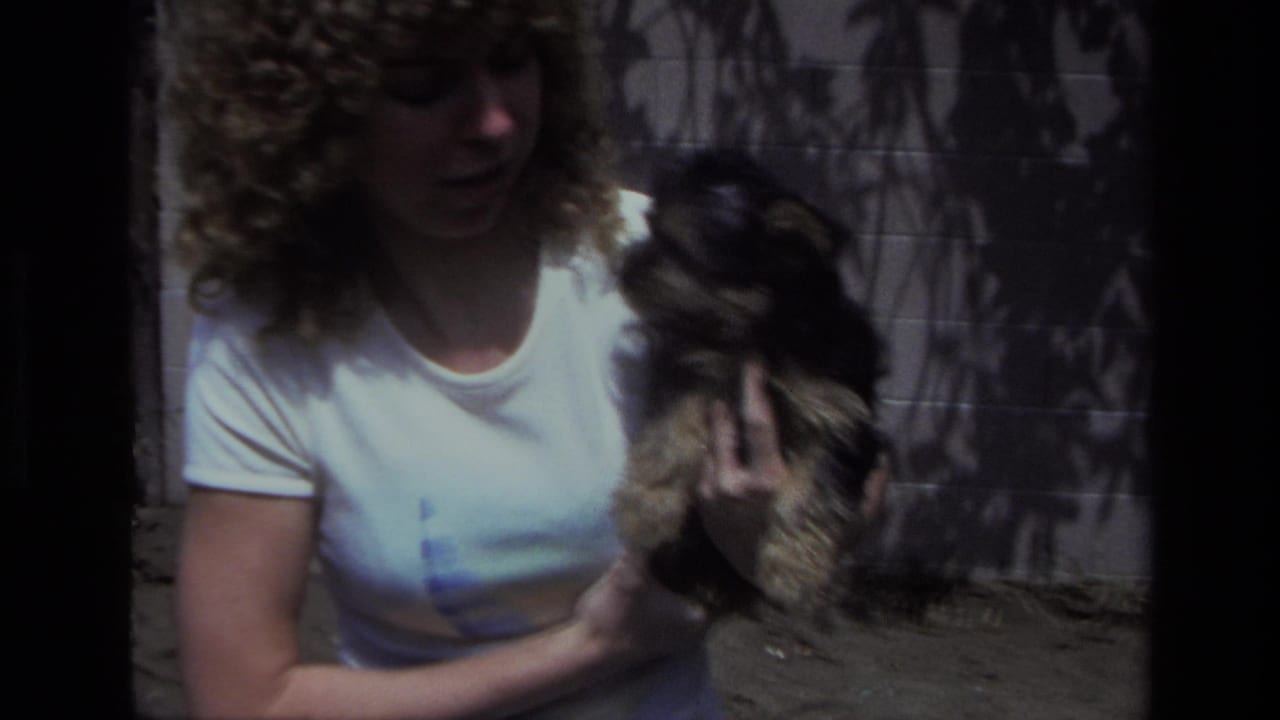 The woman holds the puppy at chest height in the Laguna Beach backyard, with the dog turned toward her face and the wall behind them.