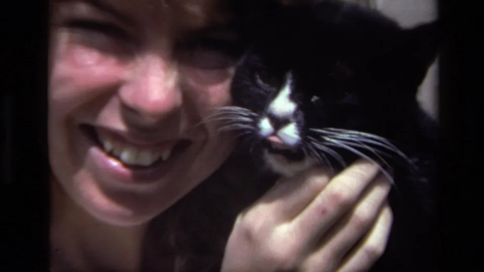 Close 8mm frame from Laguna Beach showing a smiling woman and black-and-white cat, with soft focus and strong backyard sunlight.