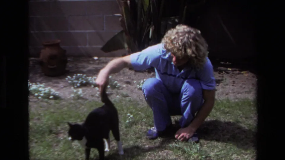 The man remains crouched in the Laguna Beach yard as the black-and-white cat begins to move away across the grass.