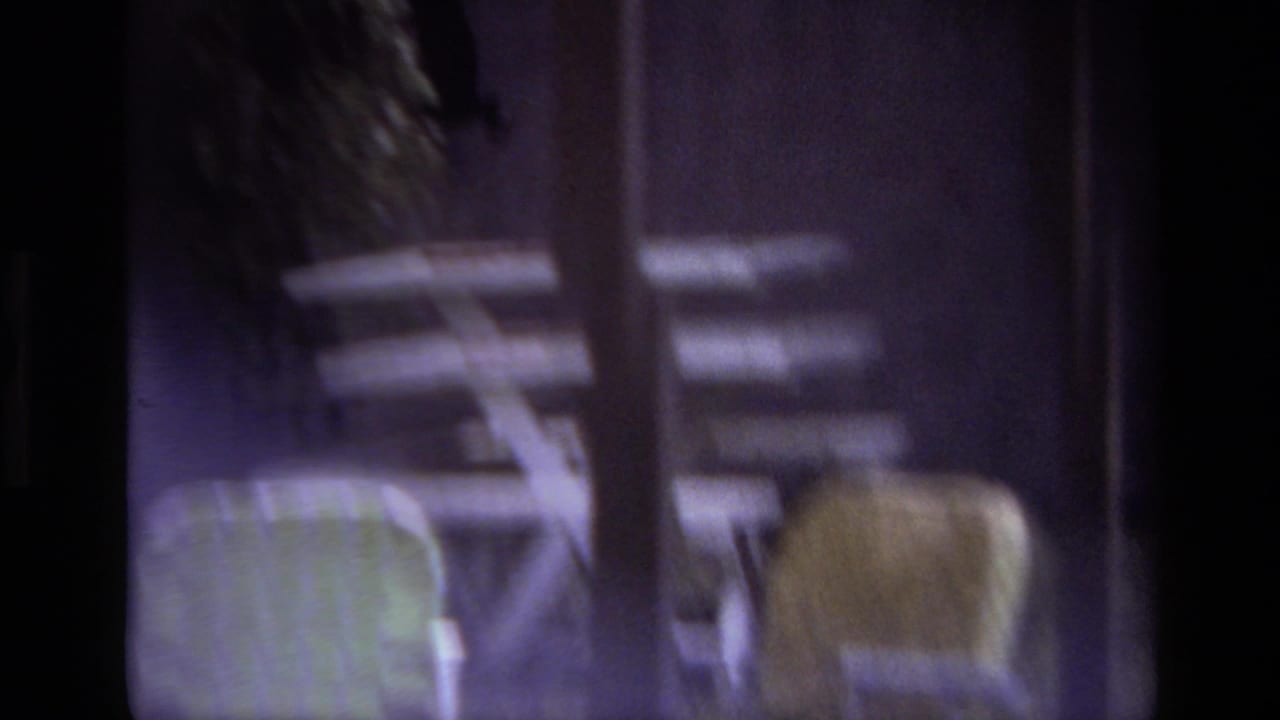 Blurred patio chairs and garden furniture seen through a dark-framed opening.