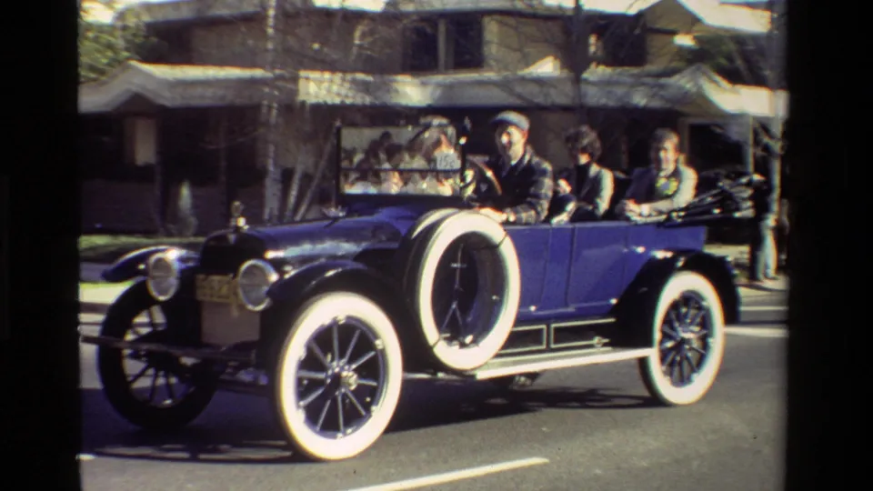 A blue antique open-top car with whitewall tires passes spectators during a California parade, supported by the 1981 clip metadata.