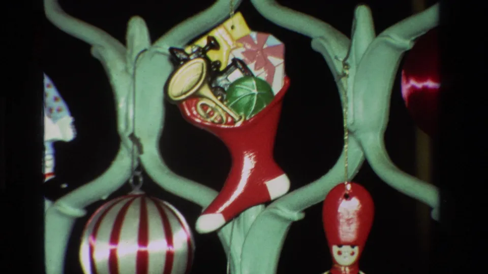 8mm home-movie frame from 1981 California showing Christmas ornaments clustered around a red stocking filled with small toys.