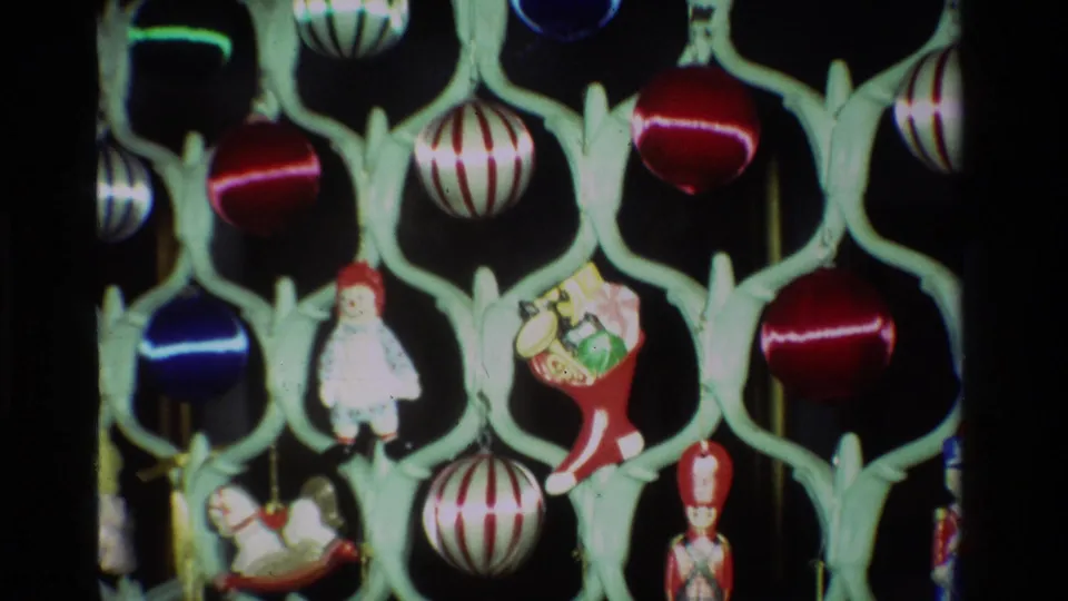 1981 California 8mm frame showing red, blue, and striped Christmas baubles with small figurines on a pale green lattice stand.
