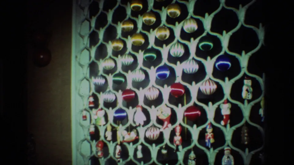 1981 California home-movie frame of a pale lattice Christmas display filled with round ornaments and small character figures.