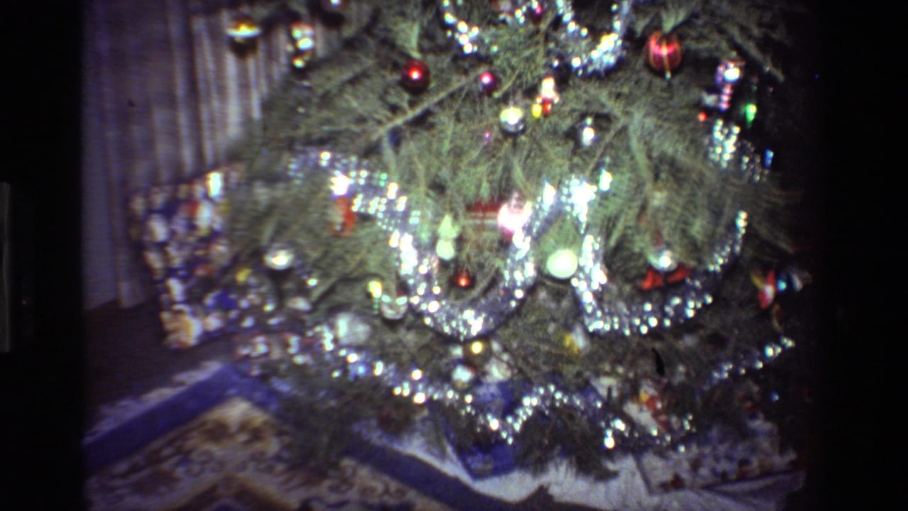 1981 California 8mm home-movie frame showing a decorated Christmas tree with silver tinsel, baubles, curtains, and gifts below.