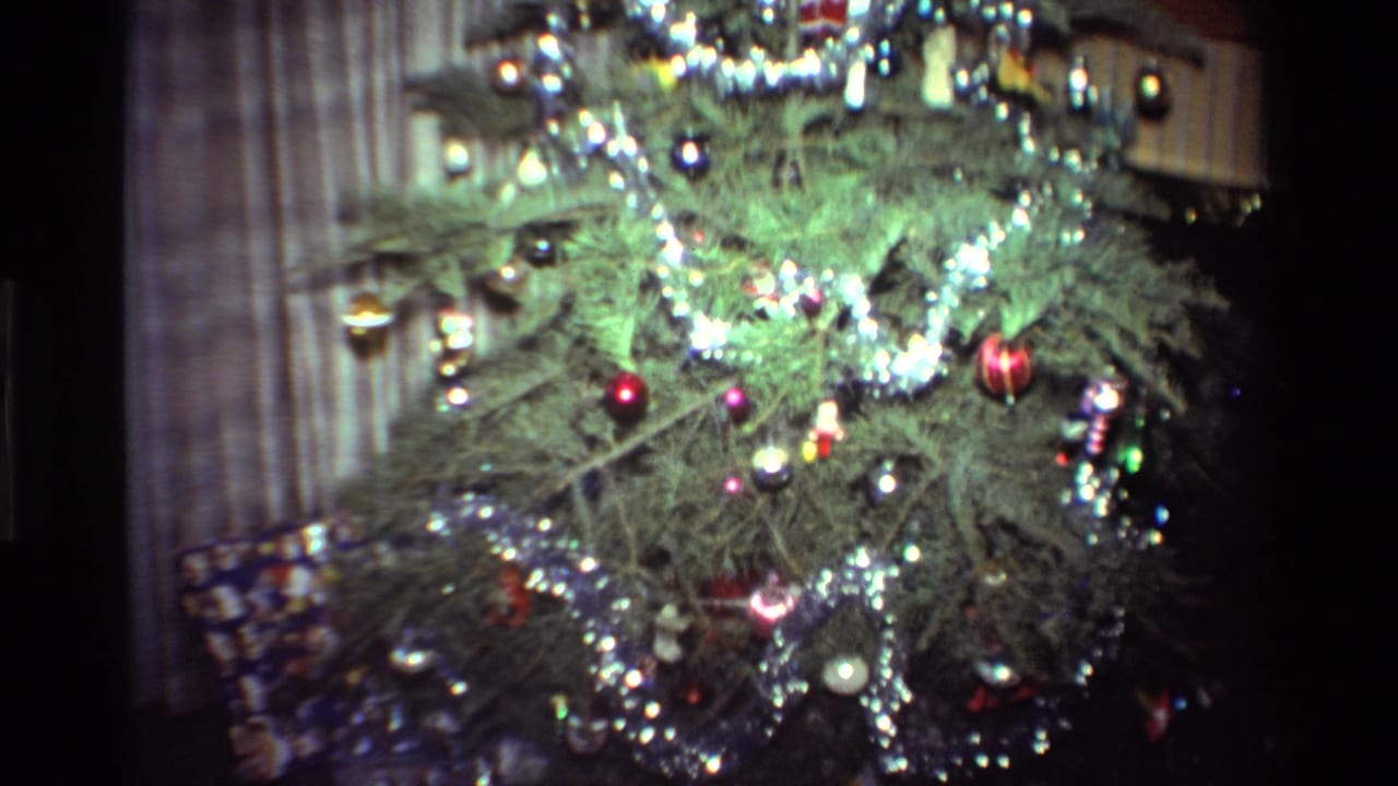The camera moves closer to the 1981 California living-room Christmas tree, showing dense tinsel, baubles, and soft home-movie color.
