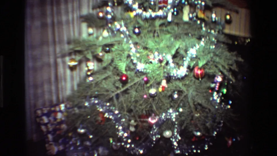 The camera moves closer to the 1981 California living-room Christmas tree, showing dense tinsel, baubles, and soft home-movie color.