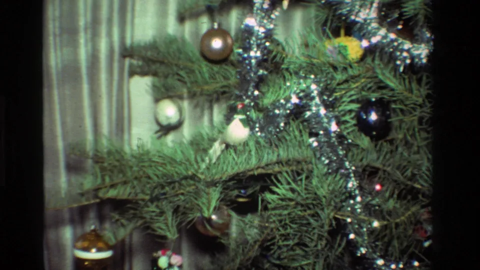1981 California 8mm frame showing Christmas tree branches with round ornaments, silver tinsel, and soft interior light.