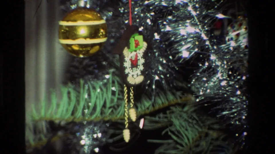 1981 8mm close-up of a gold striped bauble, a small novelty hanging ornament, tinsel, and pine branches.