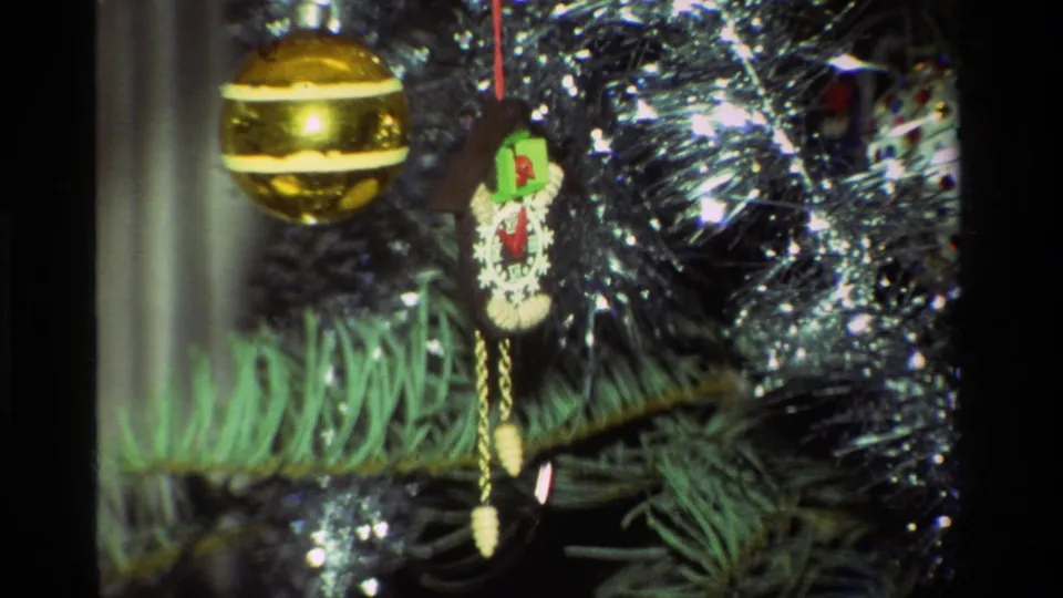 1981 California 8mm close-up of a Christmas tree with a shiny gold ball, cuckoo clock ornament, green needles, and silver tinsel.