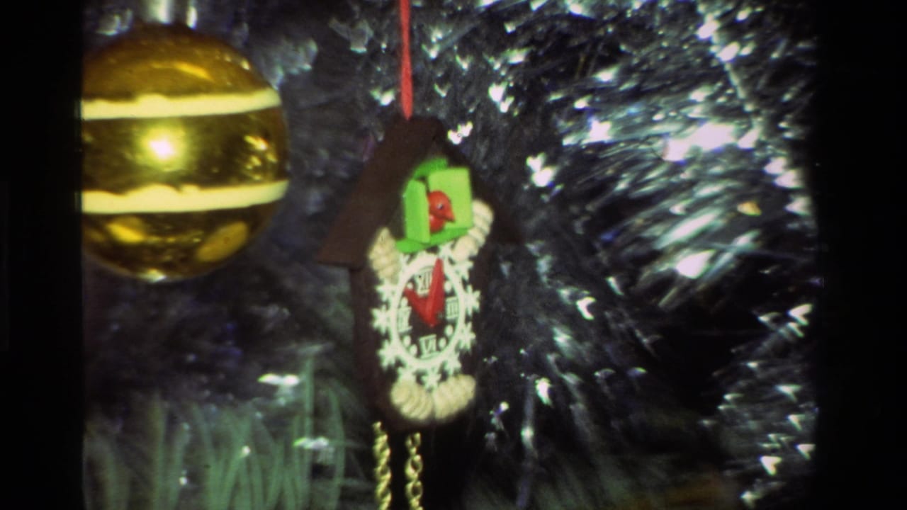 Closer view of the gold ball and cuckoo clock ornament hanging against silver tinsel on a Christmas tree.