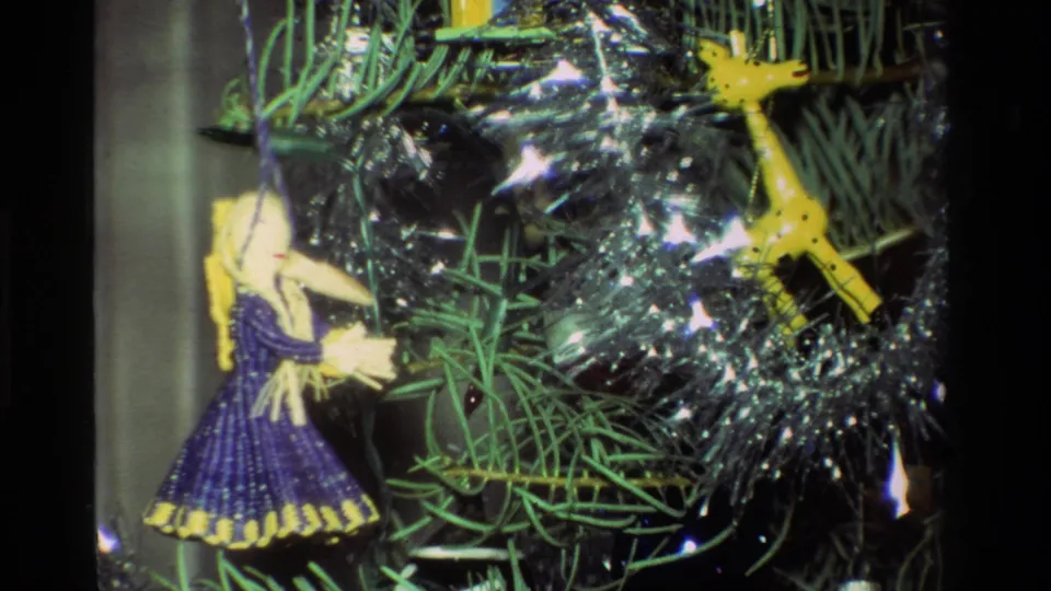1981 California 8mm close-up of beaded angel and yellow giraffe ornaments hanging among green needles and silver tinsel.