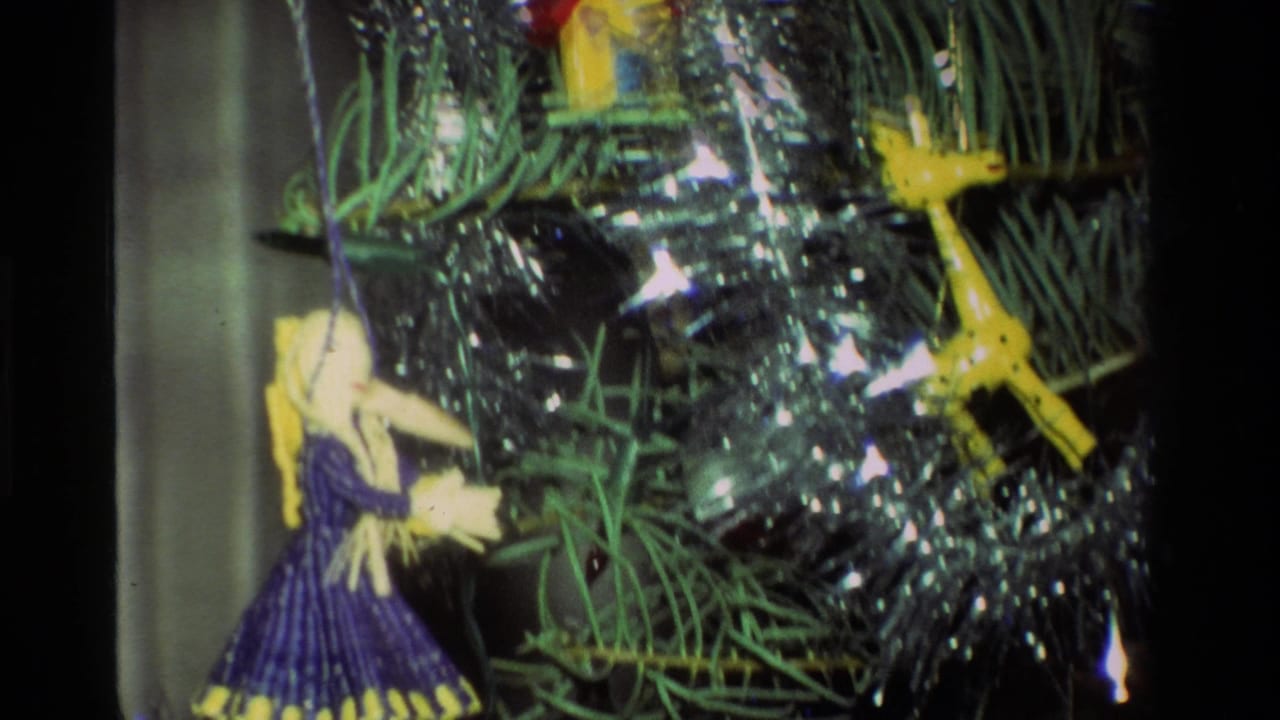 1981 California 8mm close-up of a Christmas tree with silver tinsel, a purple-dressed doll ornament, and a yellow bird ornament.