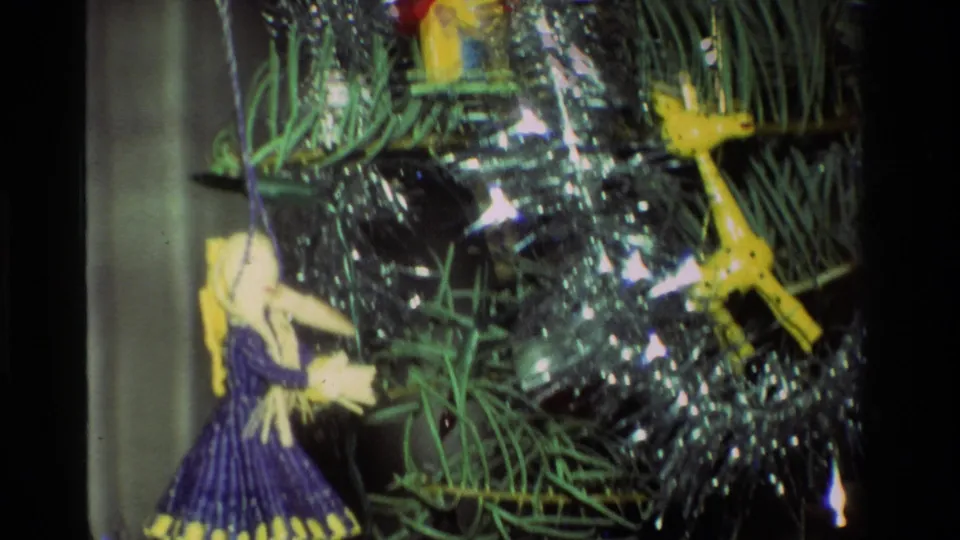 1981 California 8mm close-up of a Christmas tree with silver tinsel, a purple-dressed doll ornament, and a yellow bird ornament.
