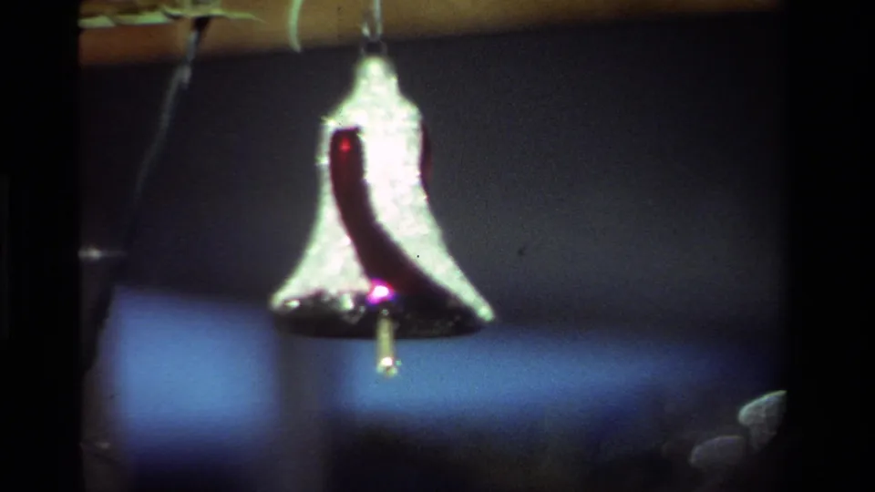 1981 California 8mm close-up of a silver bell ornament with a red accent hanging in soft indoor light.