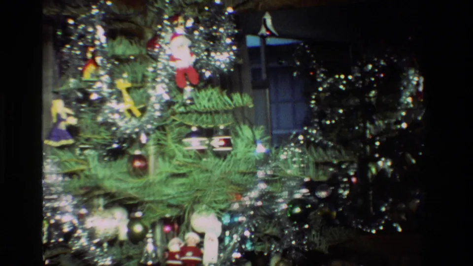 The home movie frames tree branches crowded with silver tinsel, hanging ornaments, and small decorative figures.