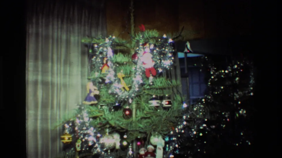 A wider 1981 California home-movie view shows the decorated Christmas tree near curtains, with ornaments and tinsel catching the light.