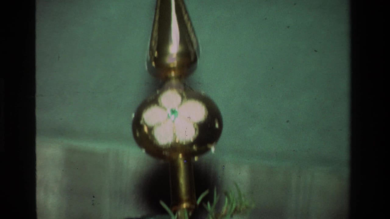 1981 California 8mm close-up of a reflective hanging ornament with a white flower motif among soft green tree needles.