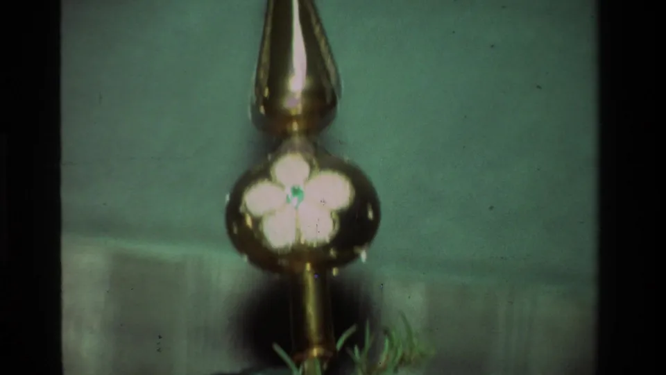 1981 California 8mm close-up of a reflective hanging ornament with a white flower motif among soft green tree needles.