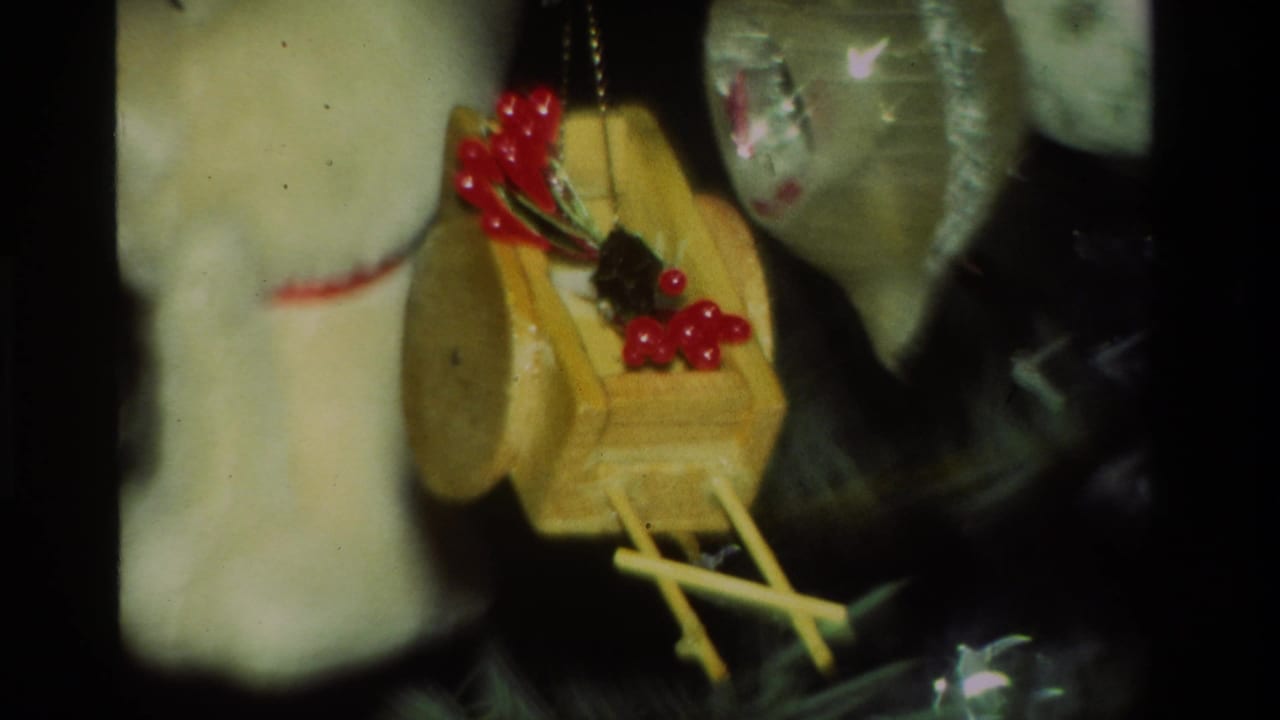 Close 8mm view of a small wooden birdhouse ornament with red berries hanging among Christmas tree decorations in California, 1981.