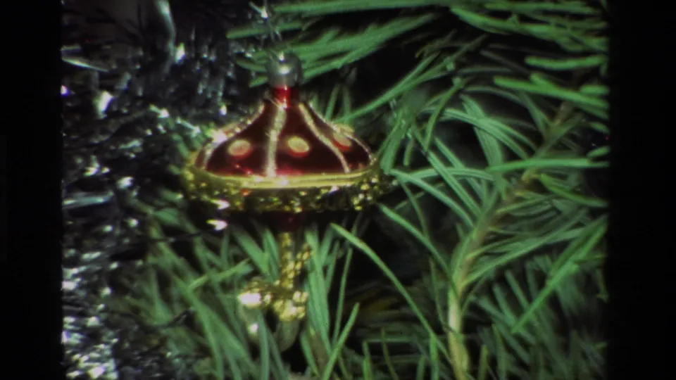 Vintage 8mm close-up of a red and gold dome-shaped Christmas ornament surrounded by pine needles and silver tinsel.