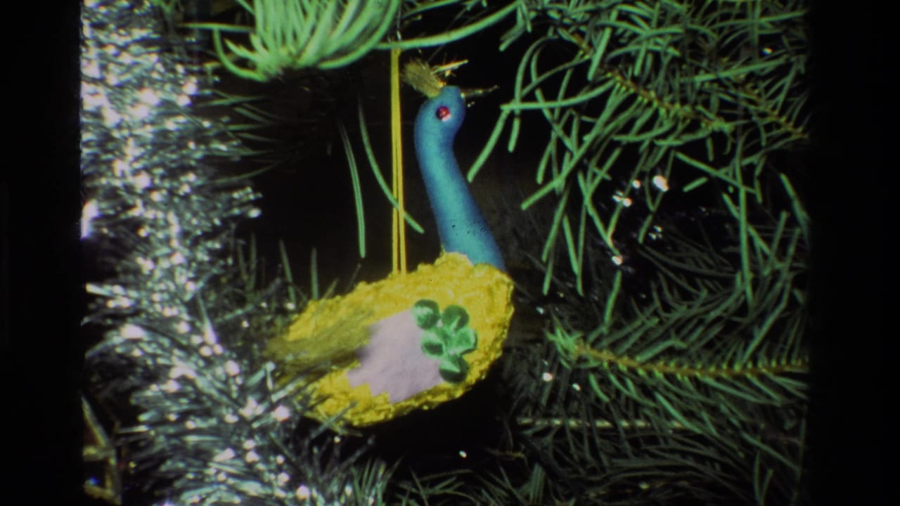 Close 1981 California 8mm frame of a blue-necked peacock-style ornament with yellow body hanging among pine needles and tinsel.