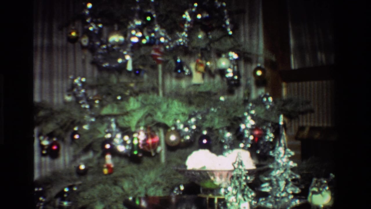 Decorated Christmas tree with tinsel, glass bulbs, small ornaments, curtains, and a window frame.
