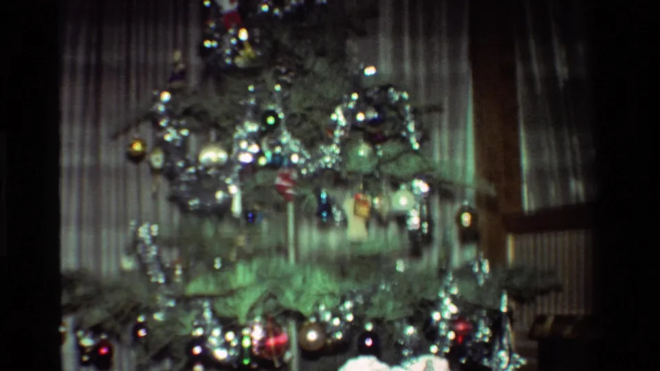 Soft 8mm frame of a California Christmas tree in 1981, with silver tinsel, hanging ornaments, curtains, and part of a window visible.
