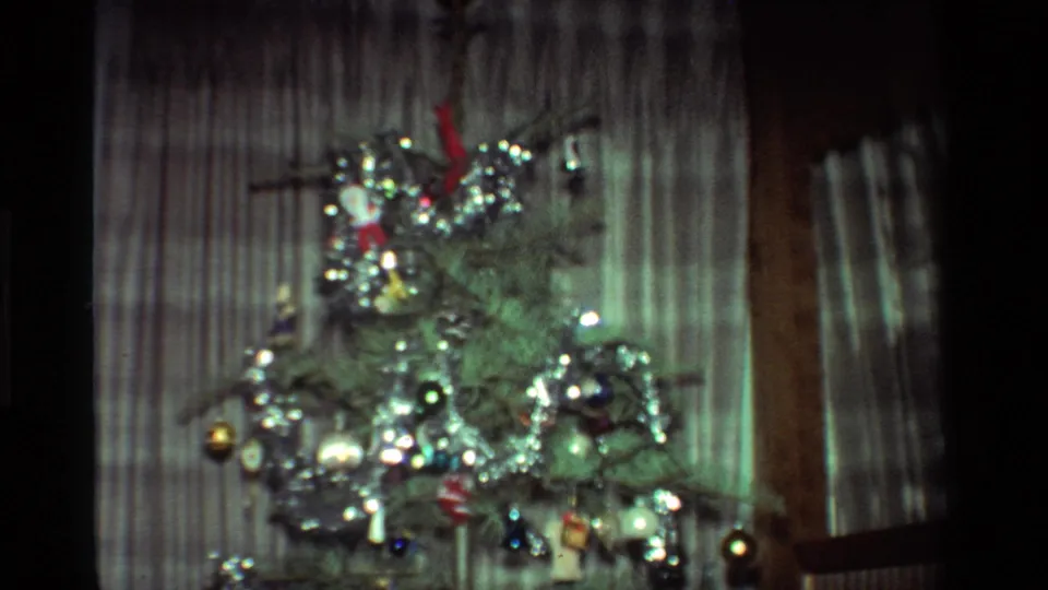 1981 California 8mm frame showing the upper area of a decorated Christmas tree with shiny tinsel, ornaments, curtains, and a wooden window frame.