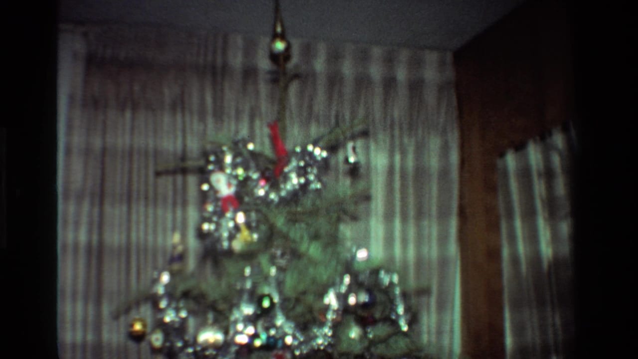 1981 California home-movie frame showing a decorated Christmas tree with silver tinsel, ornaments, and striped curtains.