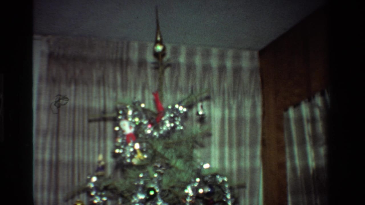 1981 California interior frame with the upper portion of a Christmas tree, tinsel, ornaments, and striped curtains.
