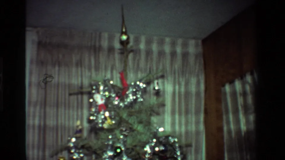 1981 California interior frame with the upper portion of a Christmas tree, tinsel, ornaments, and striped curtains.