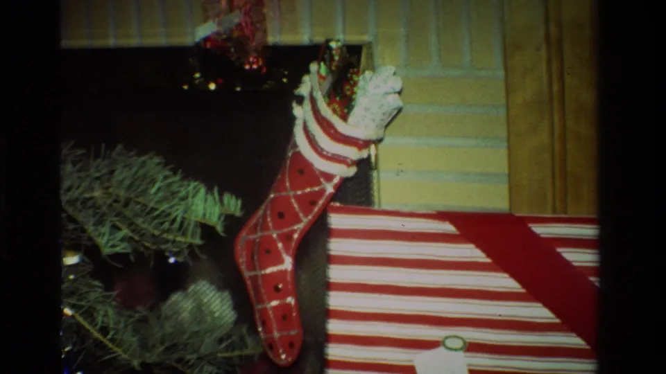 1981 California holiday interior with a stuffed red stocking, striped gift box, fireplace edge, and evergreen decoration.