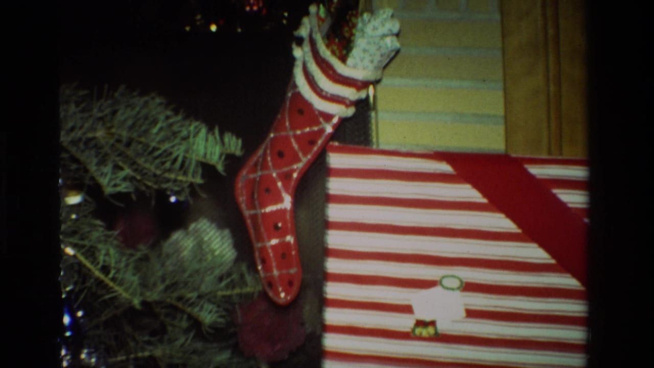 1981 California home-movie frame showing a red Christmas stocking, tree branches, ornaments, and a red-and-white striped present.