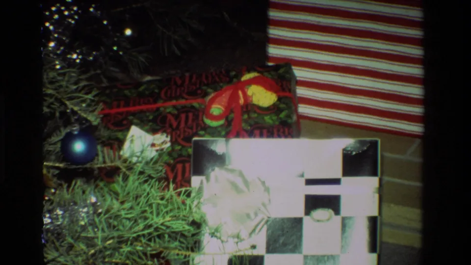 1981 California home-movie view of Christmas presents under a tree, including striped wrapping and a black-and-white checkered package.