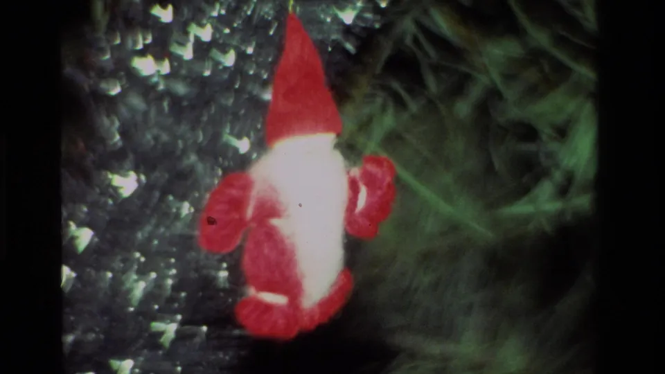 1981 California 8mm frame showing a red felt gnome ornament close to the camera among green tree needles and glittering silver material.