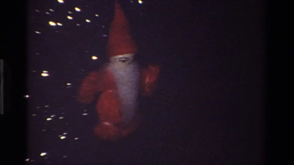 Dark Super 8 frame from the 1981 California holiday clip with the red felt gnome ornament partly lost in shadow and scattered reflections.