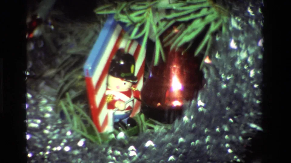 1981 California 8mm frame showing a toy soldier ornament beside a shiny red bauble, striped backing, green needles, and silver holiday trim.