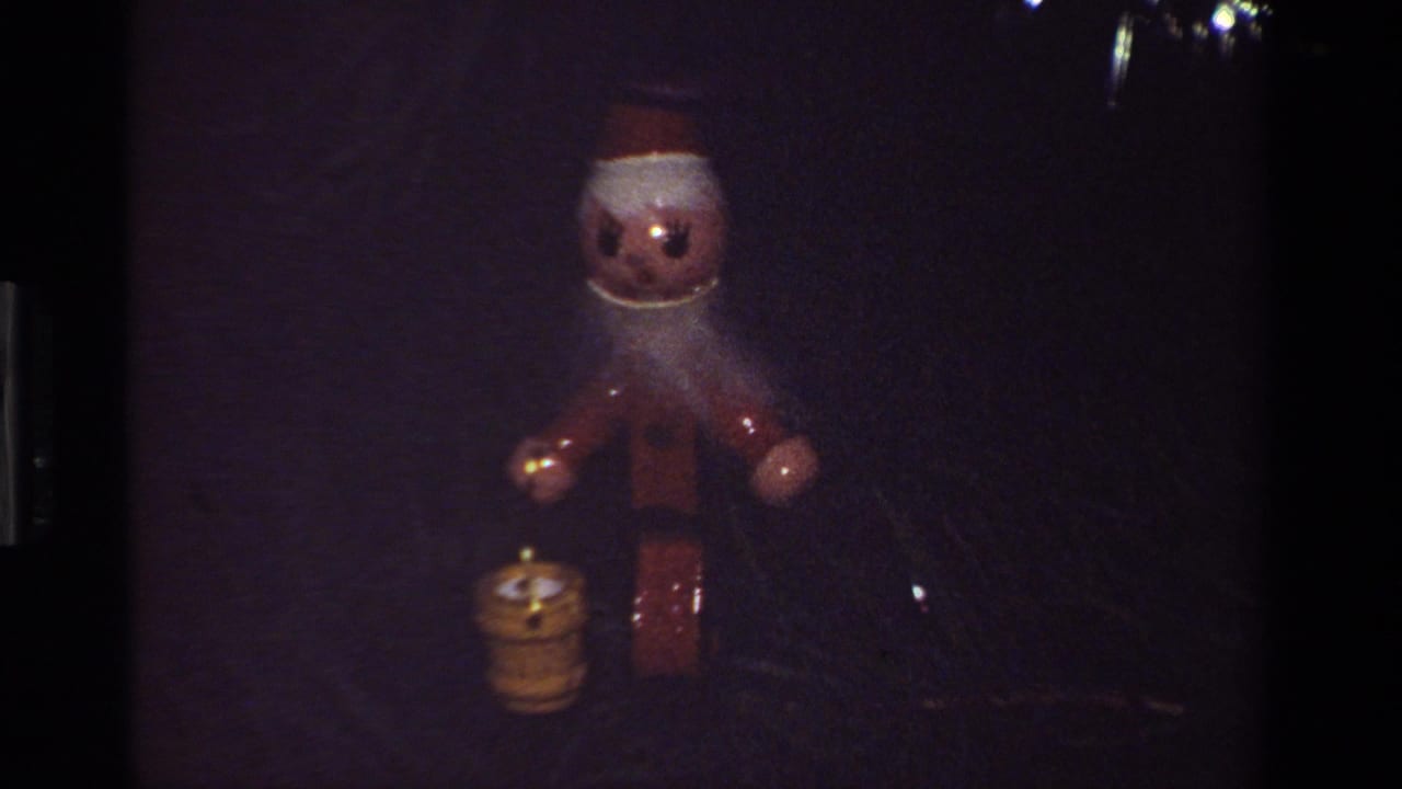 Wooden Santa ornament and small candle decoration hanging in a dark Christmas tree.
