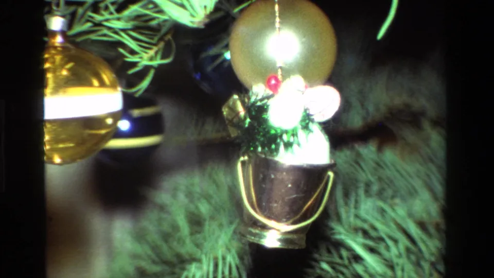 Close 1981 California 8mm shot of gold baubles and a small bucket-shaped ornament with green tinsel on a Christmas tree.
