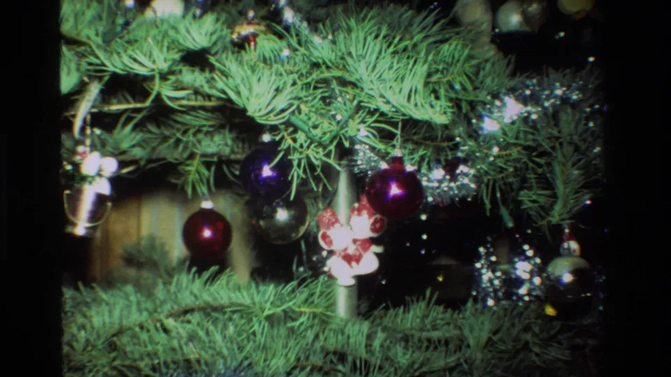 1981 California 8mm close-up of red and purple baubles, silver tinsel, and small character ornaments on a decorated Christmas tree.
