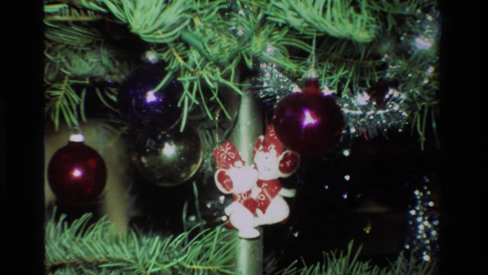 Close 1981 California 8mm frame of glossy baubles, silver tinsel, and small red-white ornaments among green Christmas branches.