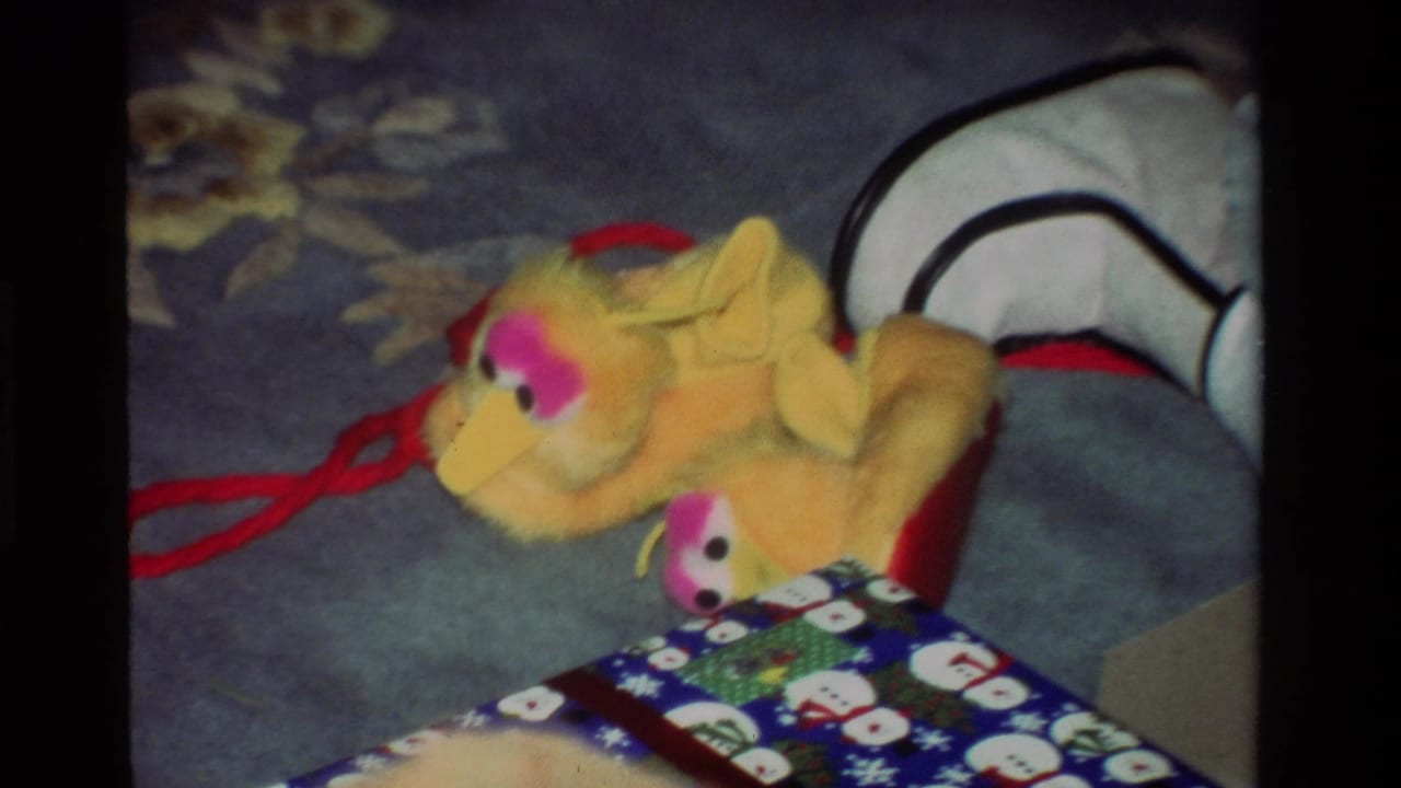 A yellow Big Bird-like plush toy lies on a blue floral carpet in a 1981 California home, near a red stocking and holiday wrapping.